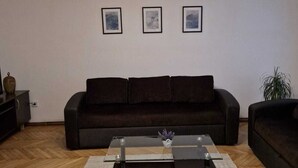 Un salon avec un canapé marron foncé, une table basse en verre et trois tableaux encadrés accrochés au mur.