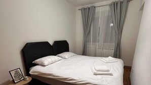 Une chambre à coucher avec un lit, une table de chevet, un luminaire suspendu et une fenêtre avec des rideaux.