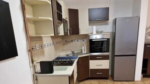 Une cuisine compacte équipée d’une cuisinière à gaz, d’un four et d’un réfrigérateur encastré. On y trouve une table à manger avec un saladier de fruits au centre.