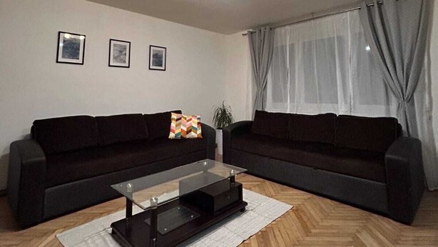 Un salon moderne avec un canapé sombre, une table basse en verre et un parquet en bois disposé en chevrons.