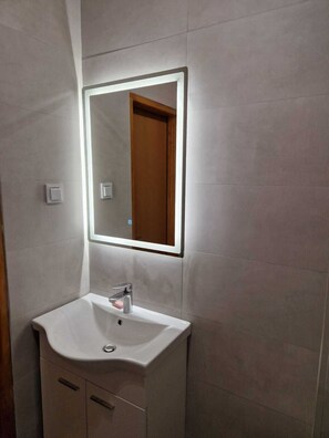 Un bagno con un lavandino bianco, uno specchio e una porta in legno.