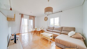 A modern living room with a sofa, a coffee table, and a dining area with chairs and a table. - AL Piso en El Poblet 3 dormitorios (El Campello)