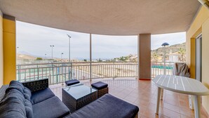 A balcony with a sofa, a small table, and a view of a beach and distant buildings. - AL Piso en El Poblet 3 dormitorios (El Campello)