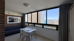 Une pièce avec une grande fenêtre, une table entourée de chaises, un canapé et un tableau encadré accroché au mur.