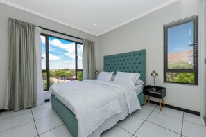 Une chambre avec un grand lit, une vue sur l’extérieur et une fenêtre équipée de stores.
