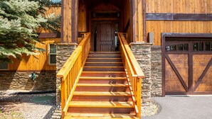 A wooden staircase leading to a door with a stone wall on one side and a garage door on the other. - PONY47 - Stunning River Front Home, Community Pool (Sunriver)