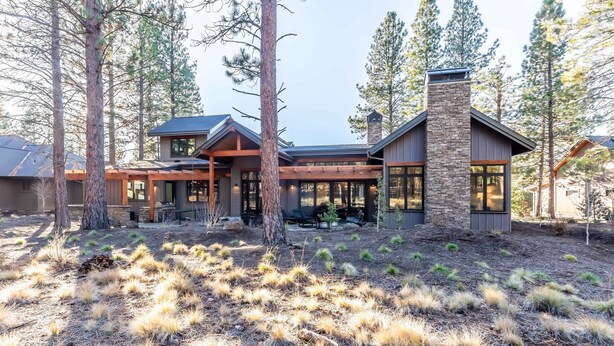 A modern house with a stone chimney, large windows, and a covered outdoor area. - SUNS93 - Gorgeous Caldera Springs Home (Sunriver)