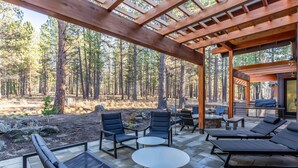 A covered outdoor patio with seating, a table, and a view of a forested area. - SUNS93 - Gorgeous Caldera Springs Home (Sunriver)