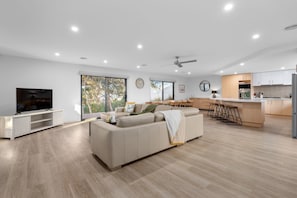 A modern living room with a flat-screen TV, a sofa, and a dining area with chairs.