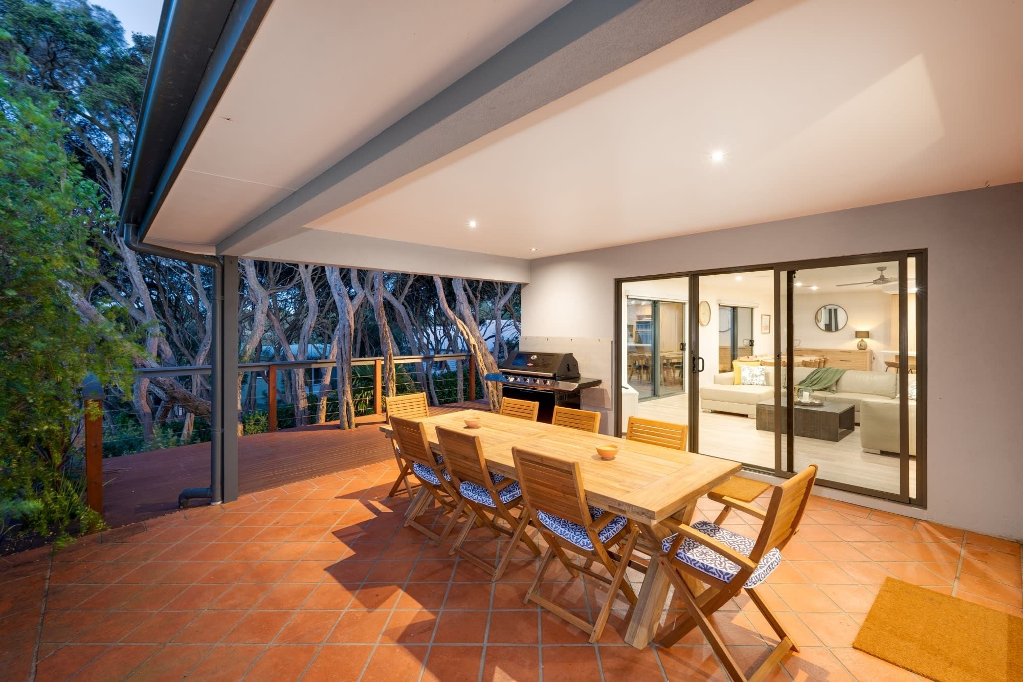 An outdoor patio with a wooden table and chairs, a barbecue grill, and a glass door leading to an interior living area.