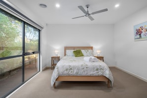 A bedroom with a bed, two bedside tables, a ceiling fan, and a large window.