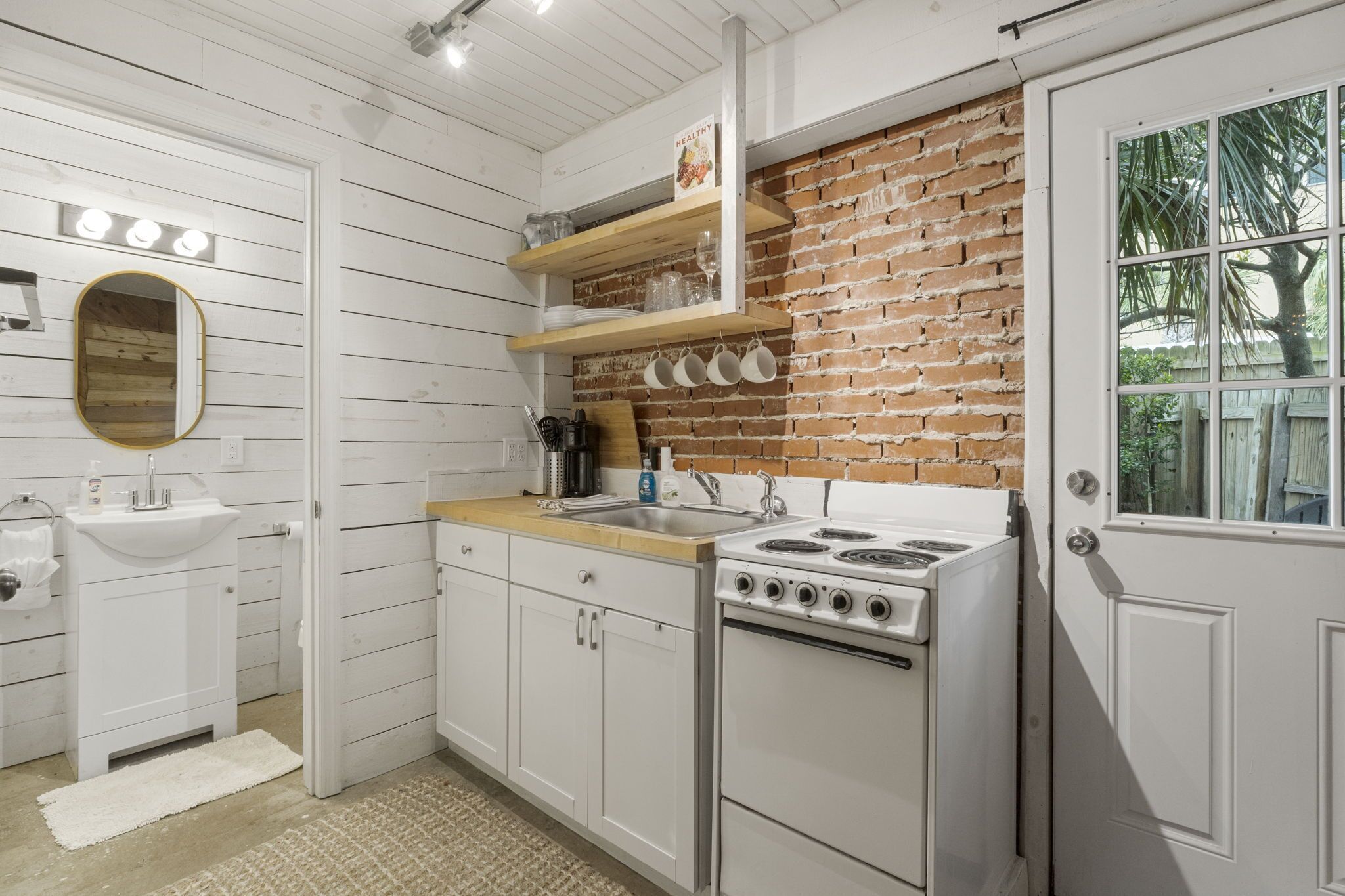 A kitchen with white cabinetry, a brick accent wall, a stove, and a sink.