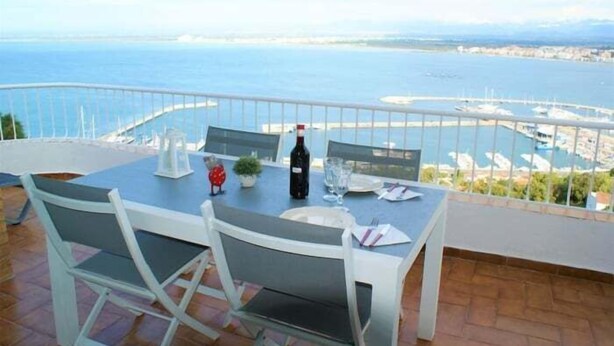 Une table à manger avec des chaises, sur un balcon donnant sur une marina et la mer.