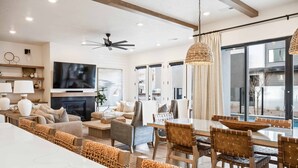 A modern living room with a large TV, comfortable seating, a dining area with a glass table, and a view of a pool through large windows. - Vinnie's Beach House: Private Pool, Lagoon + Beaches (St George)