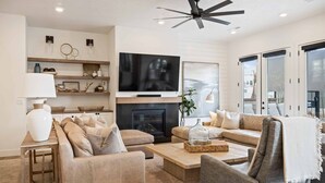 A modern living room with a fireplace, a flat-screen TV, and a ceiling fan. - Vinnie's Beach House: Private Pool, Lagoon + Beaches (St George)