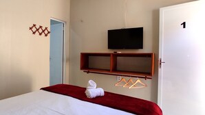 Una habitación de hotel con una cama, un televisor montado en la pared, un estante de madera y una puerta con el número 1.