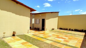 Un patio con piso de baldosas, un pequeño jardín y un edificio con techo de tejas.
