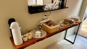 Una barra de desayuno con cafetera, tetera, tazas y una cesta de fruta.