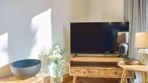 A living room with a wooden TV stand, a large flat-screen TV, a wooden side table, and a bowl on a wooden shelf. - Host & Stay | Cobnut Barn (Bonnington)