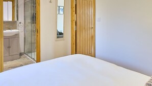 A bedroom with a large bed, a wooden door, a glass shower enclosure, and a bathroom with a sink and mirror. - Host & Stay | Oak Barn (Bonnington)