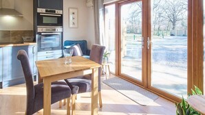 A modern kitchen with built-in appliances, a dining area with a wooden table and chairs, and a large sliding glass door leading to a view of a park. - Host & Stay | Oak Barn (Bonnington)