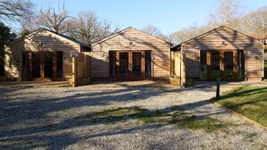 A row of three wooden cabins with large sliding glass doors, a gravel driveway, and a grassy area in front. - Host & Stay | Oak Barn (Bonnington)