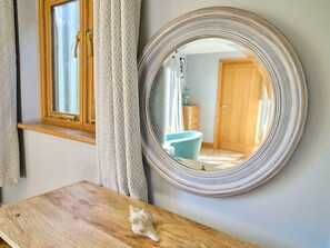 Un bany amb un envà d'estil rústic, un mirall rodó i una finestra amb cortines.