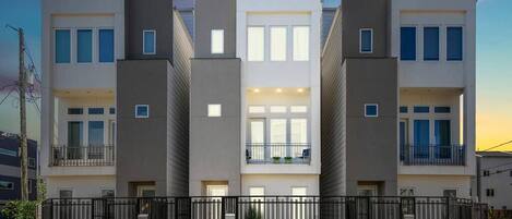 A modern multi-story residential building with balconies, a gated entrance, and a well-maintained lawn.