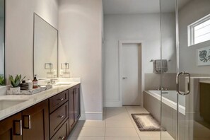 A modern bathroom with a large mirror, a bathtub, and a shower area. - Luxury Downtown Getaway With Breathtaking Views (Houston)