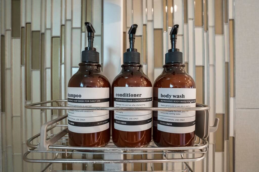 Three bottles of shampoo, conditioner, and body wash on a metal shelf.