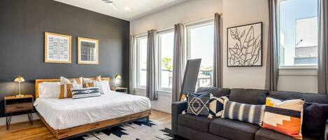 A modern bedroom with a bed, a sofa, a ceiling fan, and large windows.