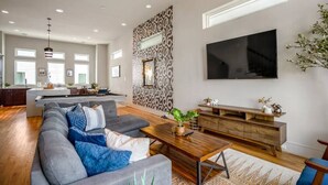 A modern living room with a large sofa, a coffee table, and a TV mounted on the wall. - Luxury Downtown Getaway With Breathtaking Views (Houston)