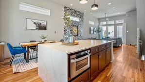 A modern kitchen with a central island, wooden cabinets, and a dining area with blue chairs. - Luxury Downtown Getaway With Breathtaking Views (Houston)