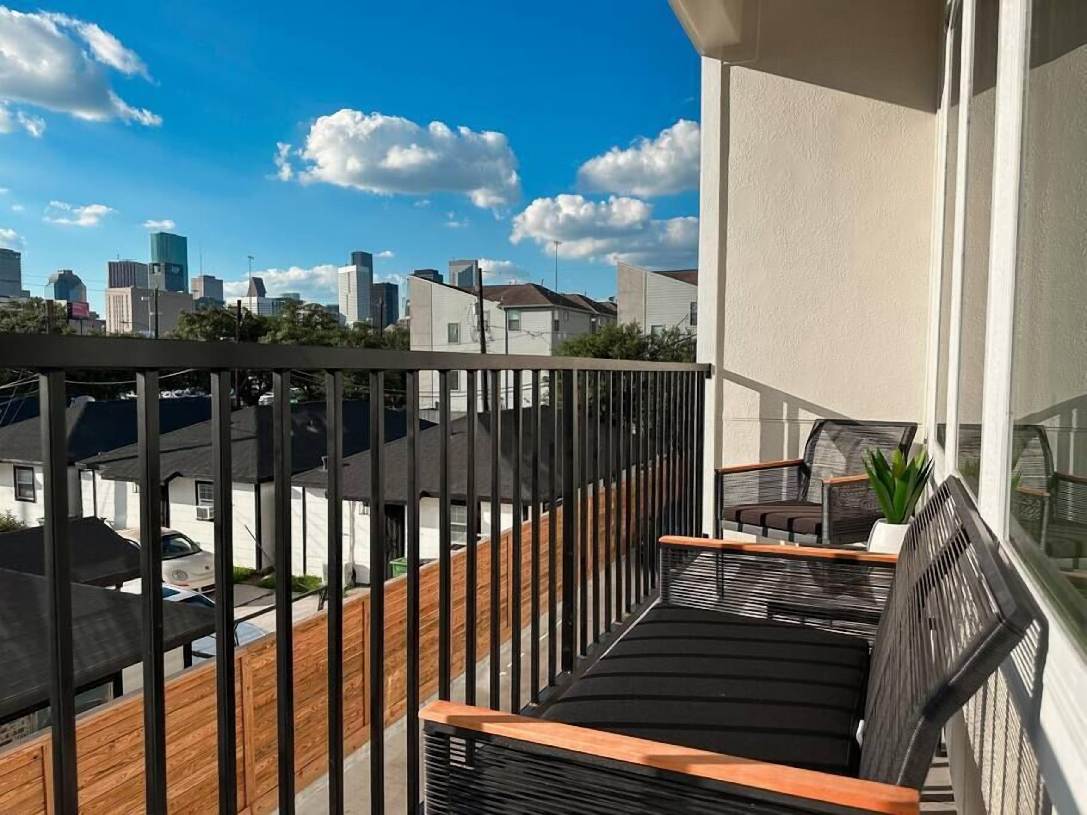 A balcony with a view of a city skyline, wooden railings, and a seating area with a potted plant.