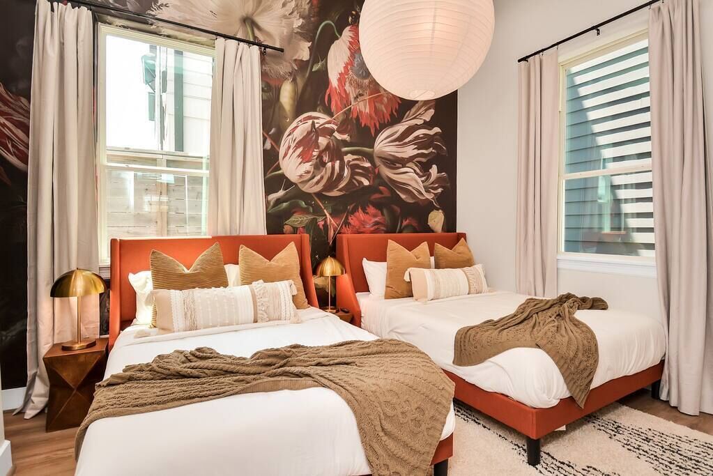 A double bed room with two beds, a large floral mural, and a hanging light fixture.