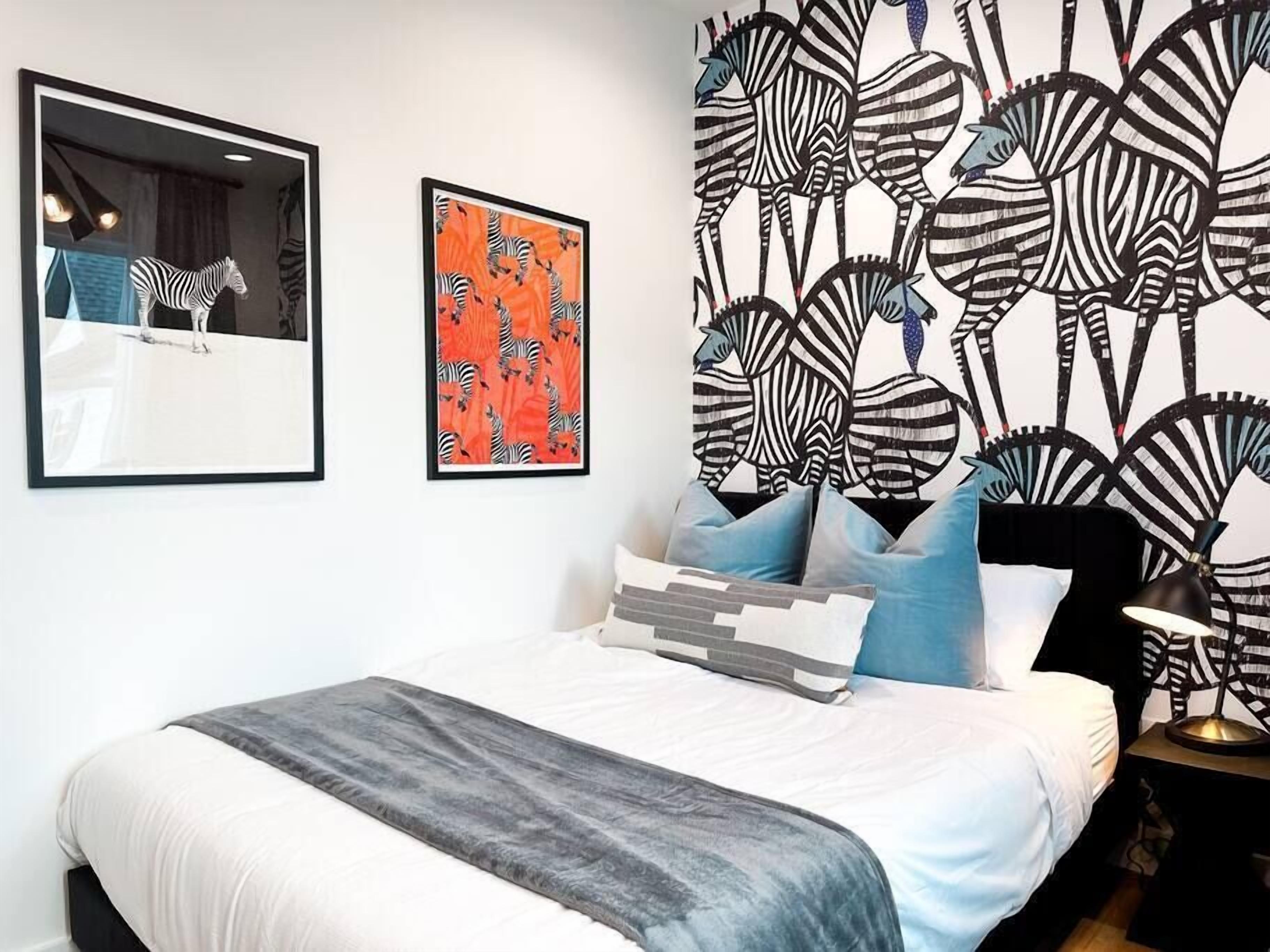 Un dormitorio con cama, almohadas, una mesita de noche y una pared con diseño de cebra.