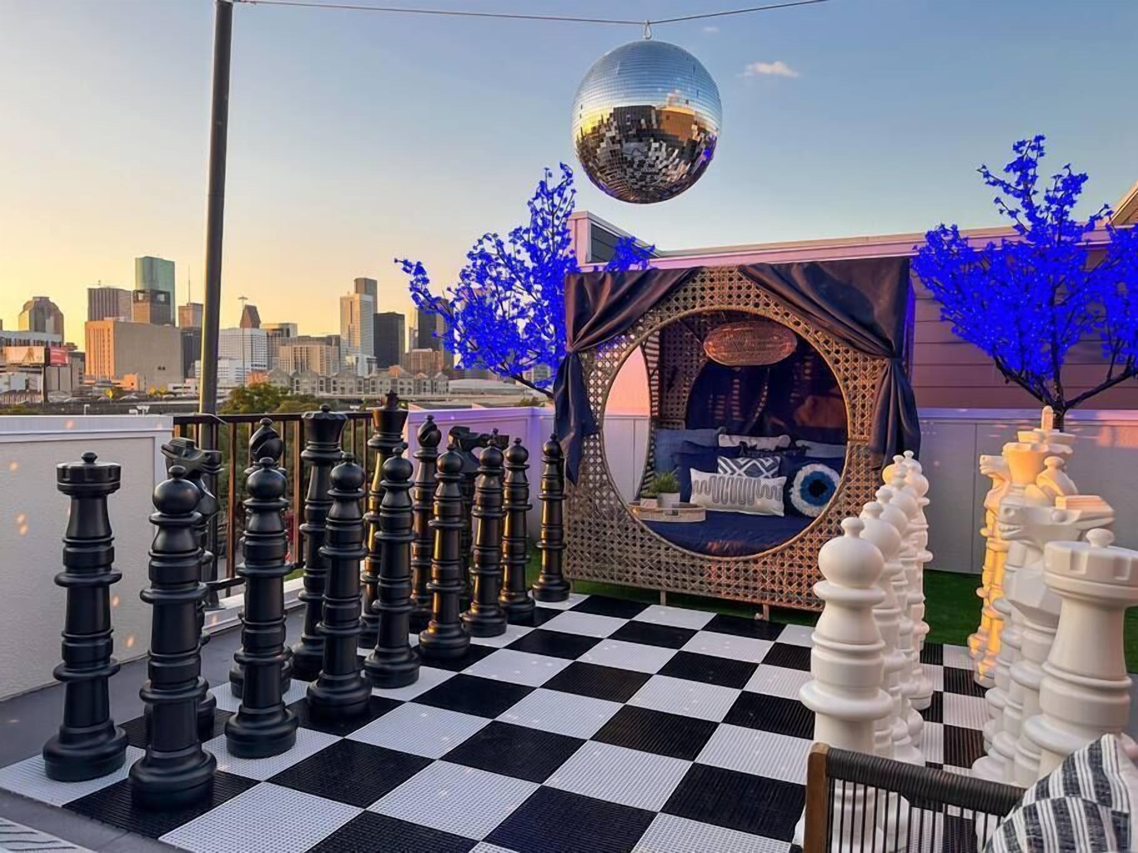 A rooftop with a chessboard, a disco ball, and a view of the city skyline.