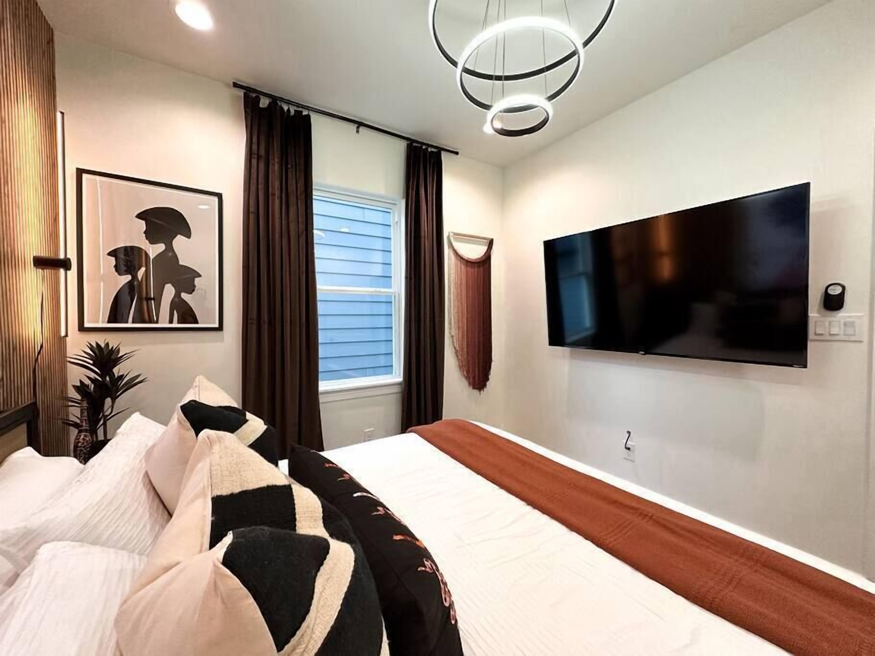 Une chambre moderne avec un grand lit, un téléviseur à écran plat fixé au mur et une fenêtre avec des rideaux.