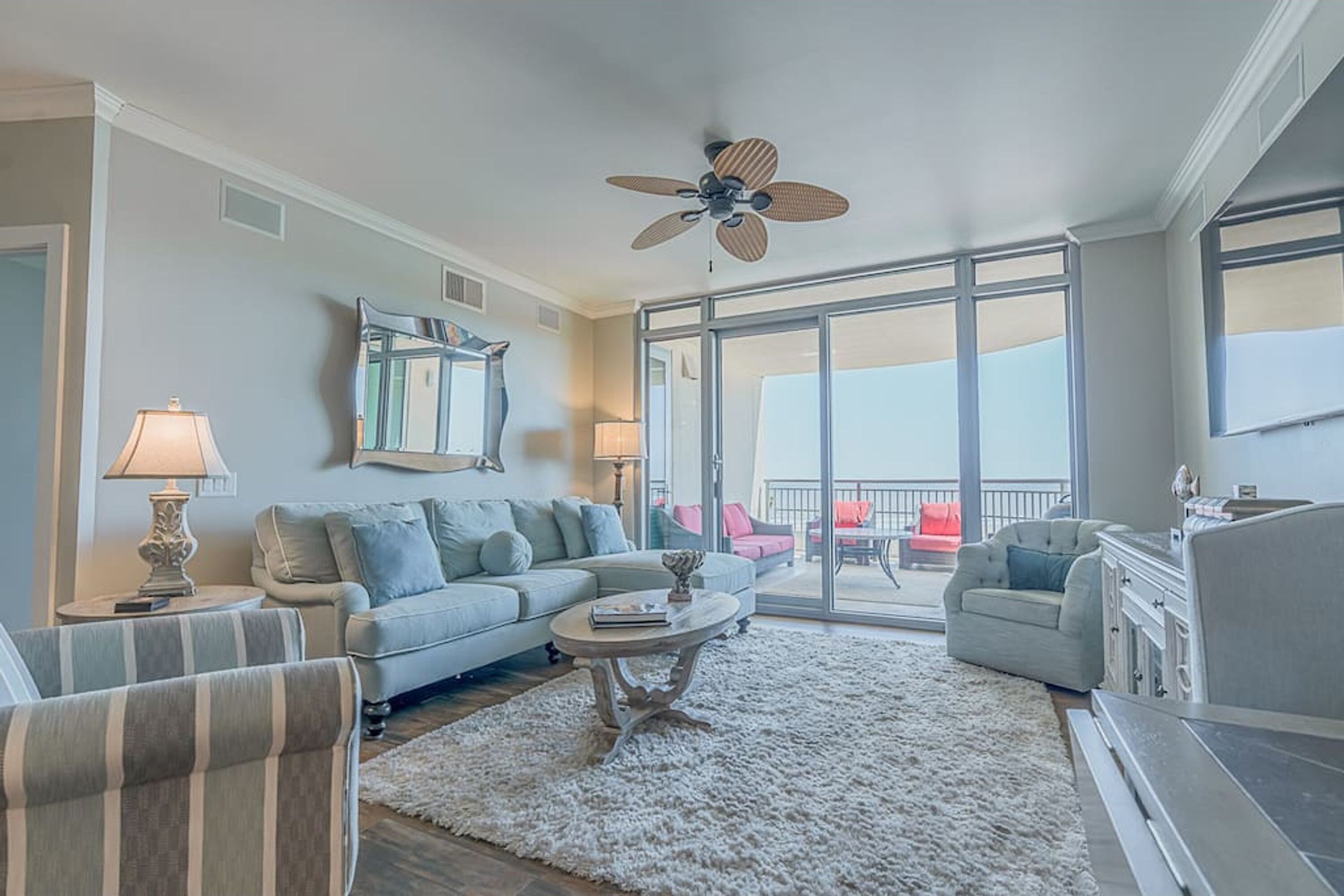 A spacious living room with a sofa, armchairs, a coffee table, and a ceiling fan.