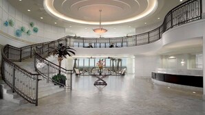 Eine geräumige Lobby mit einer zentralen Treppe, einem Empfangsschalter und einer modernen Kronleuchter.