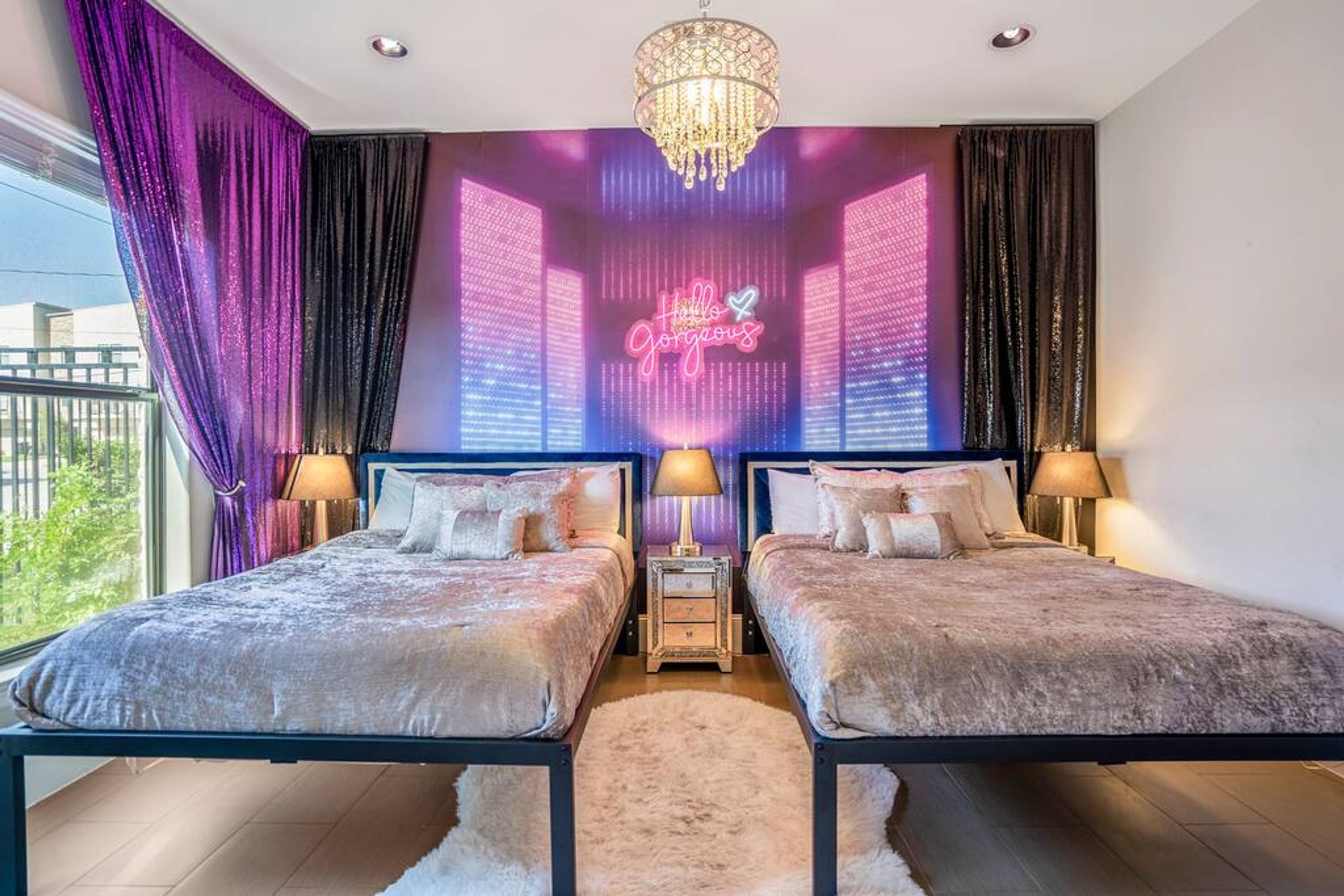 A bedroom with two beds, a chandelier, and a neon sign on the wall.