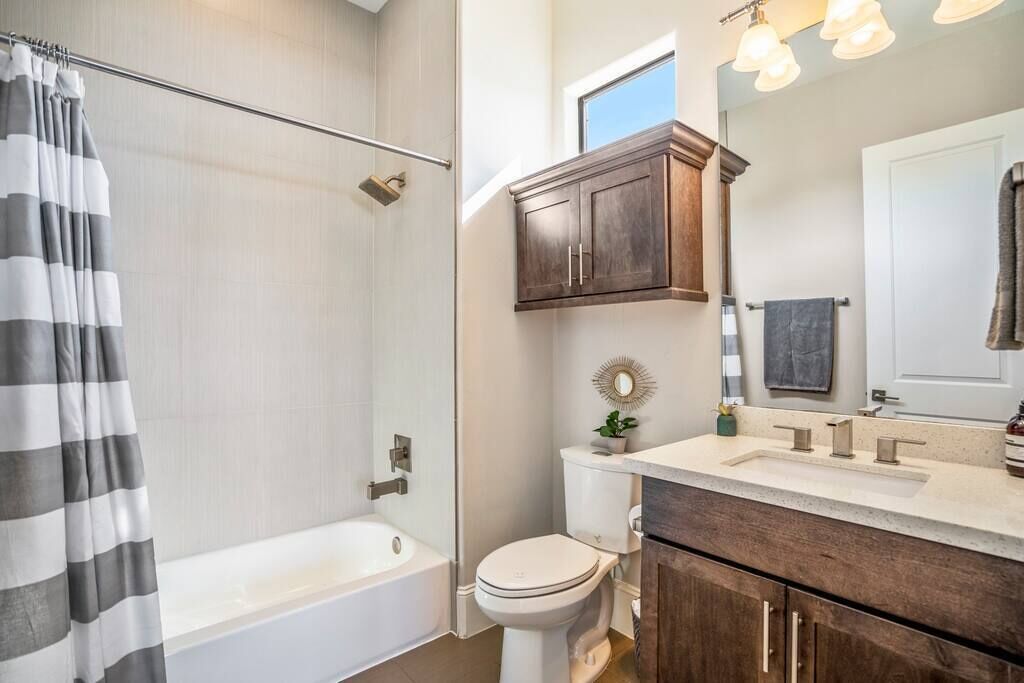 Une salle de bain équipée d’une baignoire, de toilettes, d’un meuble-lavabo avec un miroir et d’un rideau de douche.