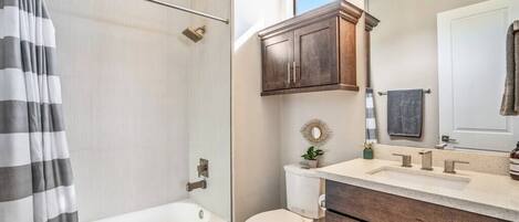 A bathroom with a bathtub, toilet, vanity with a mirror, and a shower curtain.