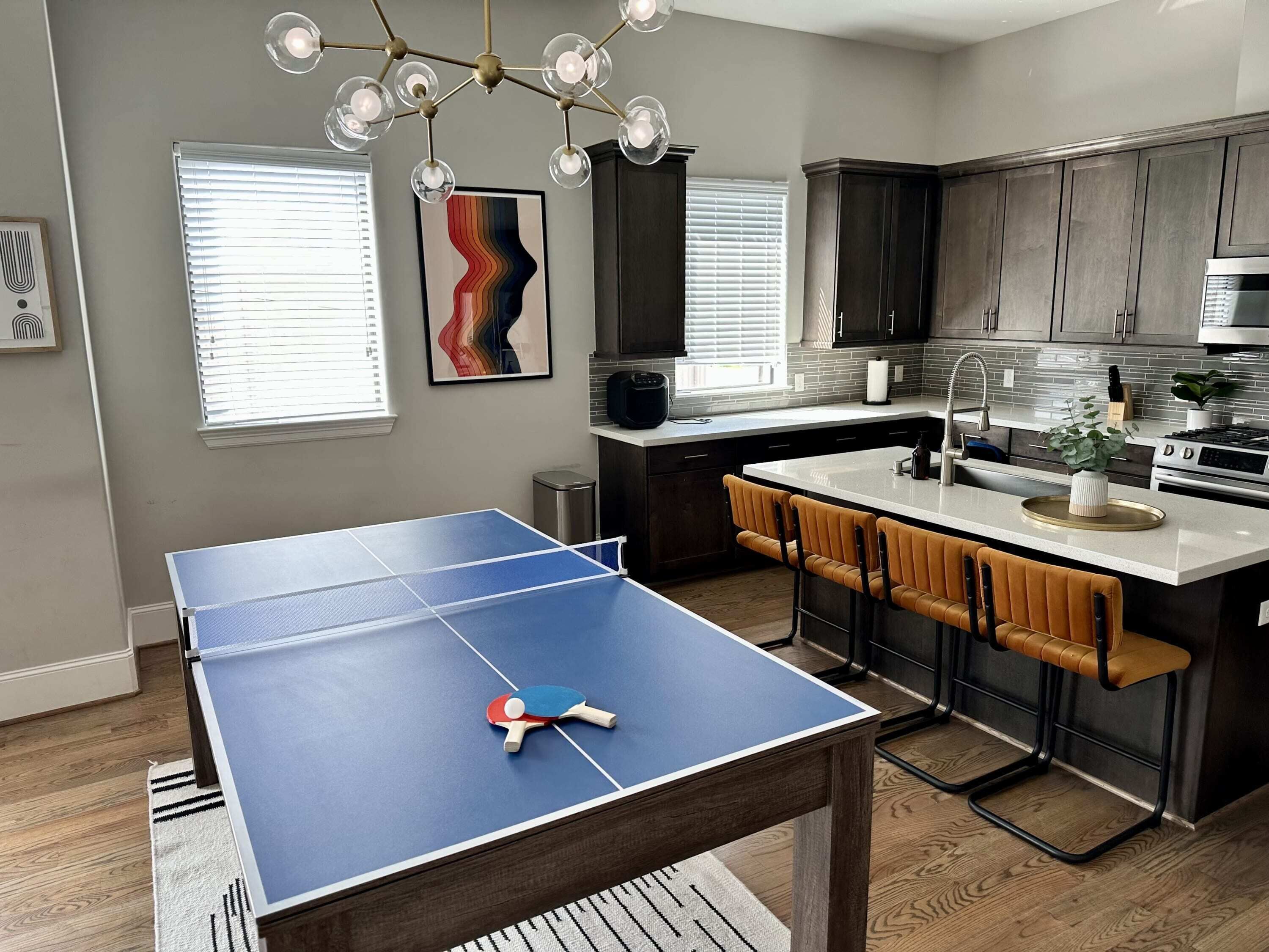 A modern kitchen with a ping pong table, bar stools, and a dining area.
