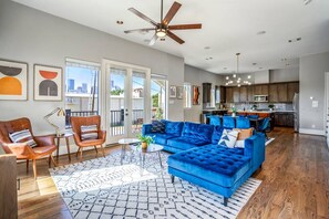 A spacious living area with a blue sofa, wooden flooring, and a city view. - Luxury Downtown Home w Rooftop Deck in the Skyline (Houston)