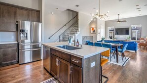 A modern kitchen with stainless steel appliances, a wooden island, and a dining area with blue upholstered chairs. - Luxury Downtown Home w Rooftop Deck in the Skyline (Houston)