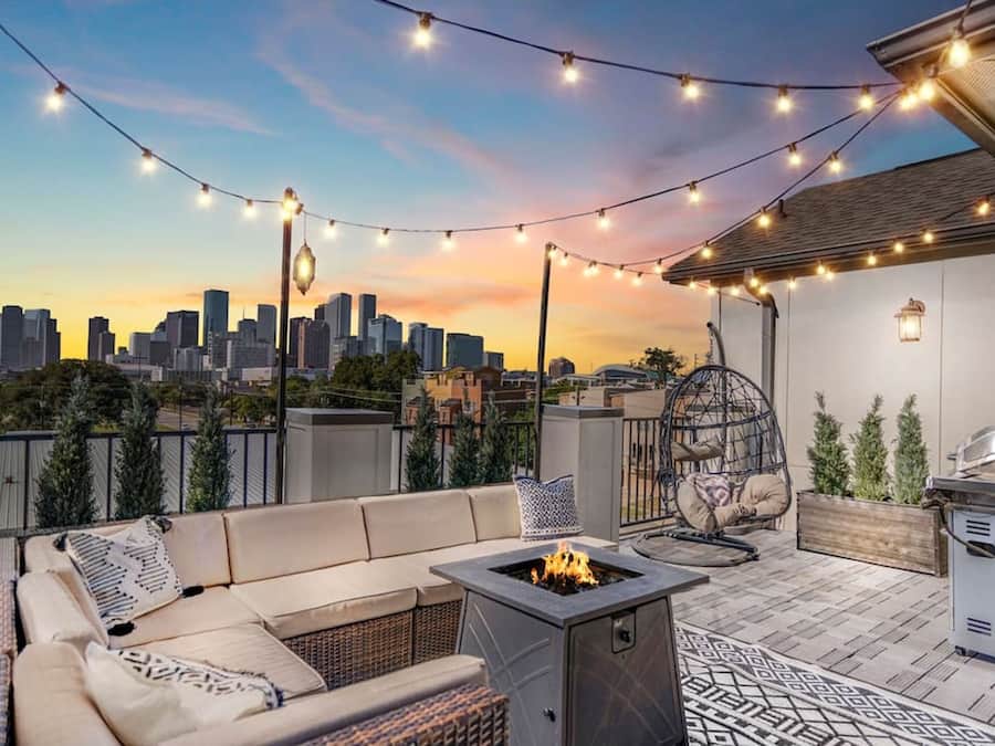 Un patio al aire libre con sofá, una chimenea, luces colgantes y una parrilla.