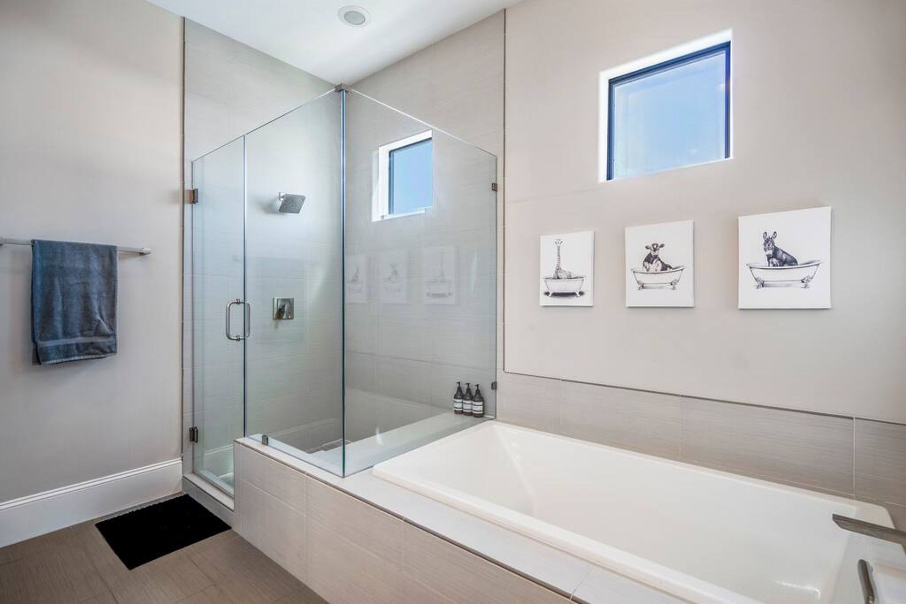 A modern bathroom with a glass-enclosed shower, a large bathtub, and three framed artworks on the wall.