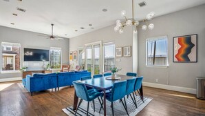 A modern living room with a blue sofa set, a dining table with blue chairs, and a chandelier. - Luxury Downtown Home w Rooftop Deck in the Skyline (Houston)