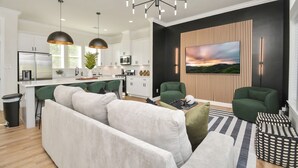 A modern living room with a sofa, green chairs, and a coffee table. There is a kitchen in the background with white cabinets and a black countertop. - Paradise Palace Best Rooftop in HTX w Hot Tub (Houston)